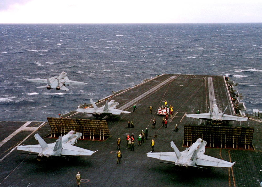 An F-14 Tomcat launches as four F/A-18 Hornets wait to launch from the USS Enterprise.