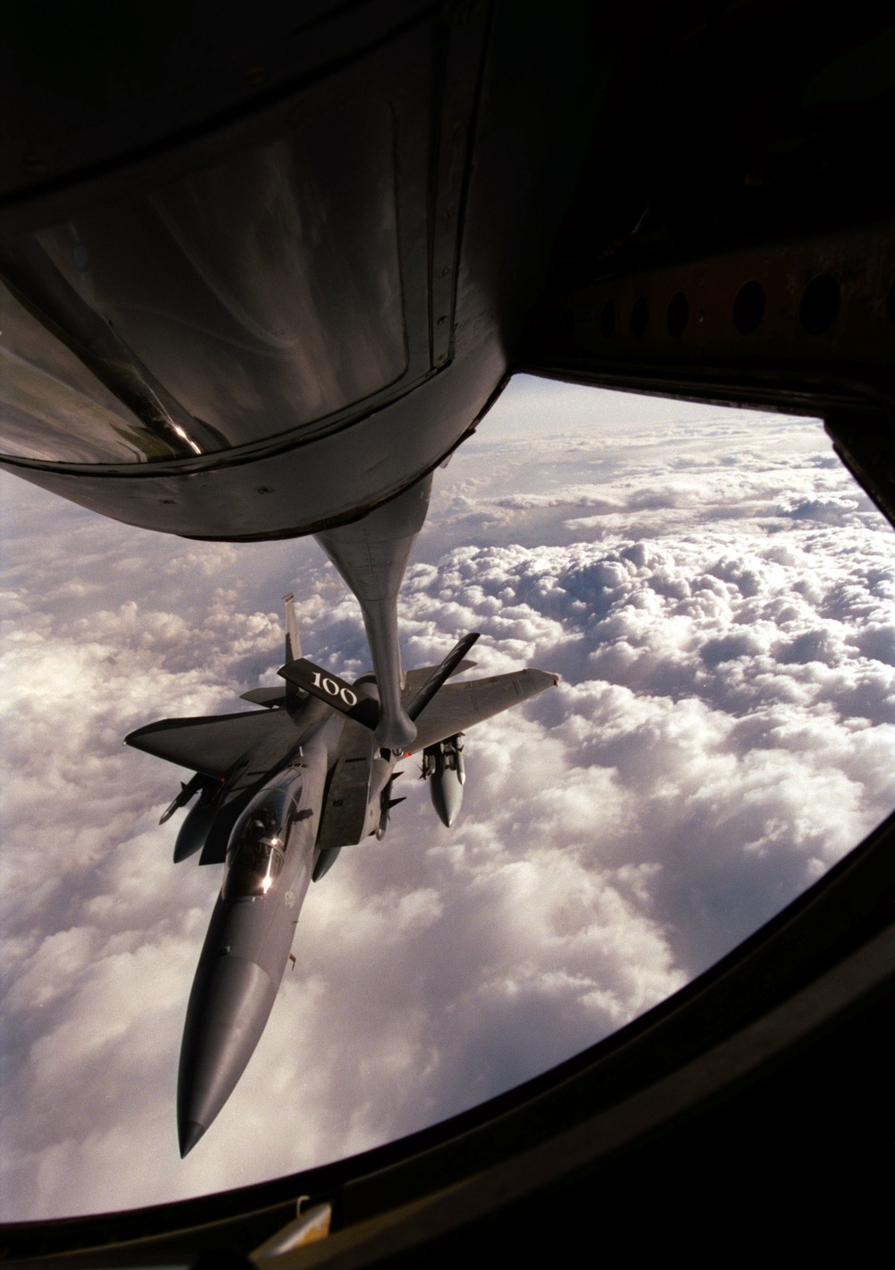 An F-15C Eagle is framed by the boom operator's window as it approaches a KC-135R Stratotanker.