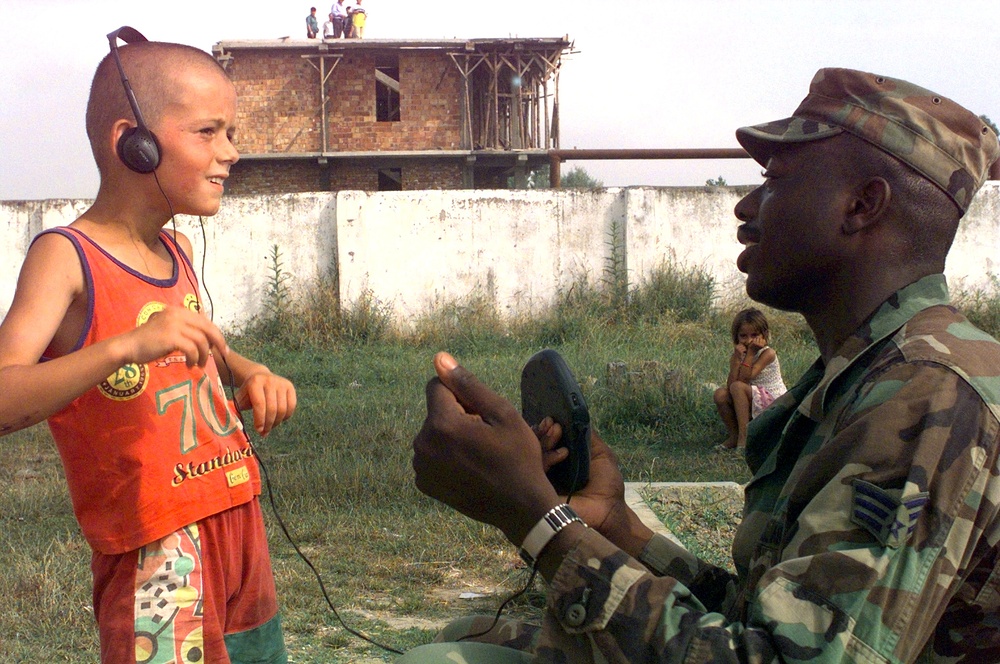 Senior Airman Justin Rhodes allows an Albanian child to listen to a compact disc player.