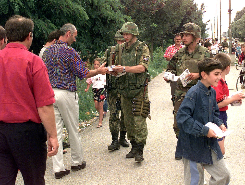 American and Russian soldiers pass out flyers to the citizens of Kamenica, Kosovo.