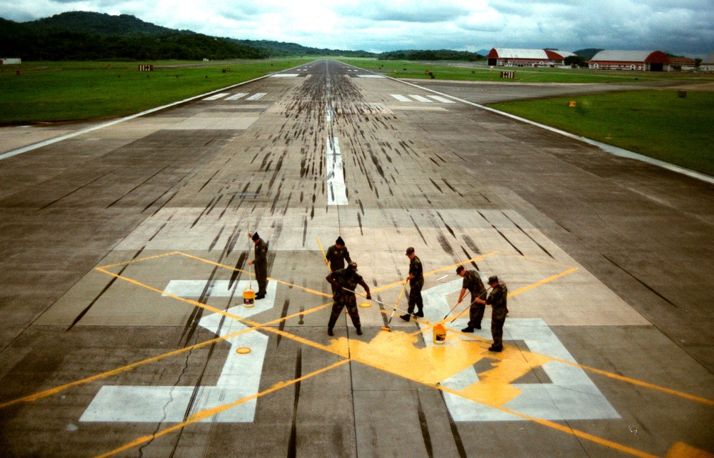 U.S. Army and Air Force personnel paint a yellow cross over the runway number at Howard.