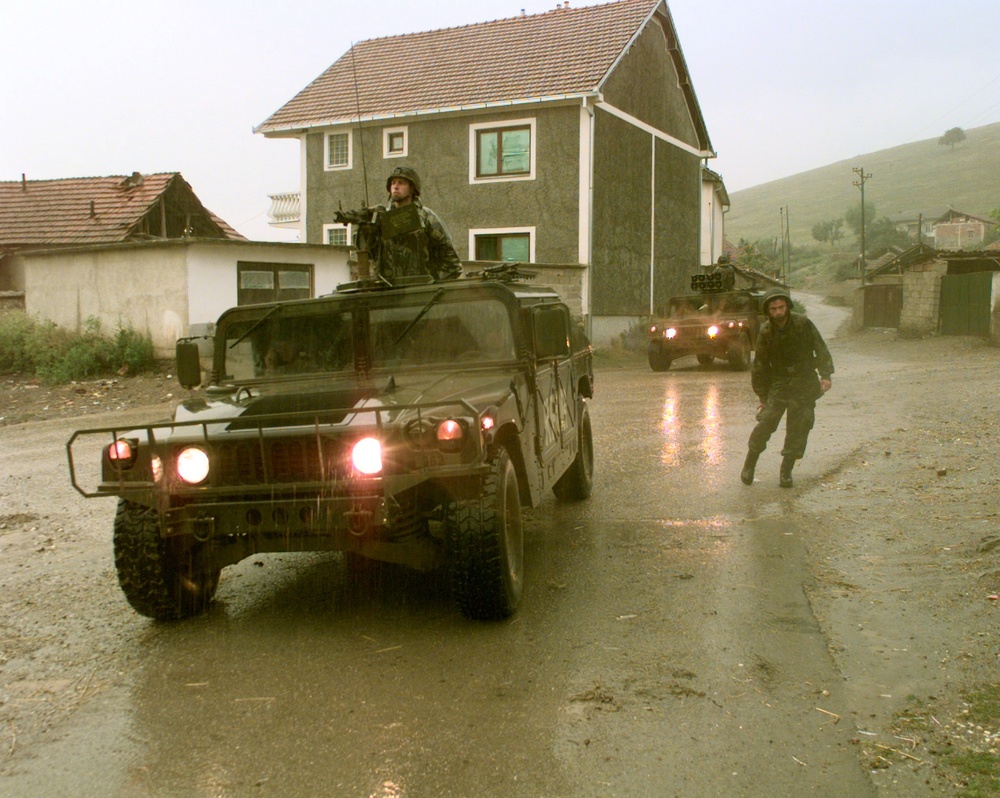 Soldiers of Alpha Company, 1st Battalion, 77th Armored Regiment wait in the rain by their Humvees.