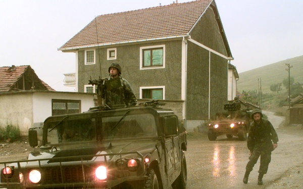 Soldiers of Alpha Company, 1st Battalion, 77th Armored Regiment wait in the rain by their Humvees.