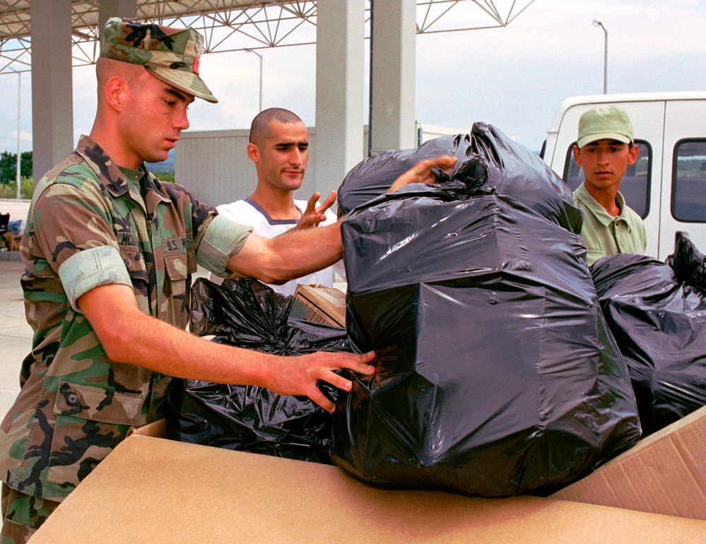 A U.S. Marine and two Turkish sailors load bags of hygiene supplies into a cargo box.