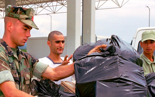 A U.S. Marine and two Turkish sailors load bags of hygiene supplies into a cargo box.