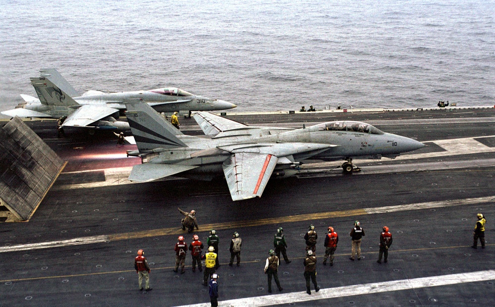 Flight deck personnel watch as an F-14 Tomcat hits the afterburner before launching from the aircraft carrier USS Kitty Hawk (CV 63).