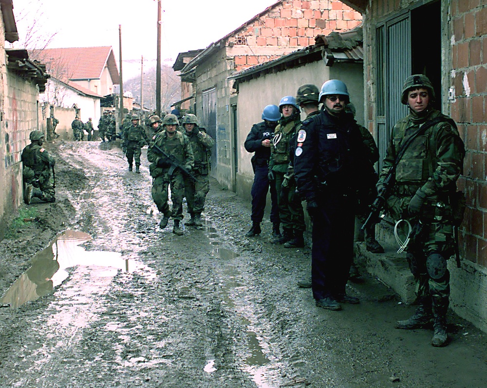 Soldiers from the 504th Parachute Infantry Regiment and United Nations' police move down a muddy alley way in Mitrovica, Kosovo.