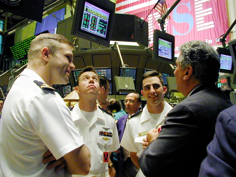 Bull Ensigns Pete Sommers, Eric Sadler, and Benjamin Andrew talk with a trader on the floor of the New York Stock Exchange.