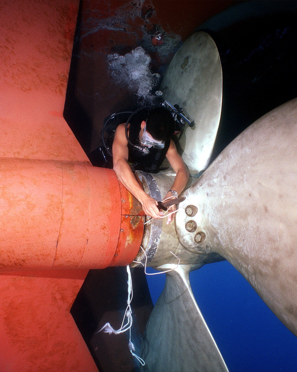 Navy Diver Benjamins uses his dive knife to cut away heavy gauge fishing line to free the fouled propeller of the USS Grasp.
