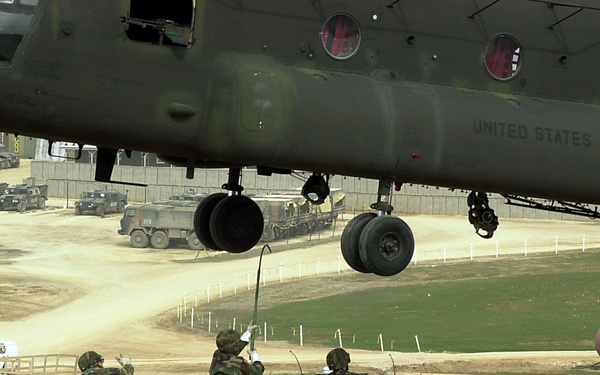 A soldier reaches up to touch a CH-47 Chinook helicopter as he and his fellow soldiers prepare to sling load a container from Camp Bondsteel.