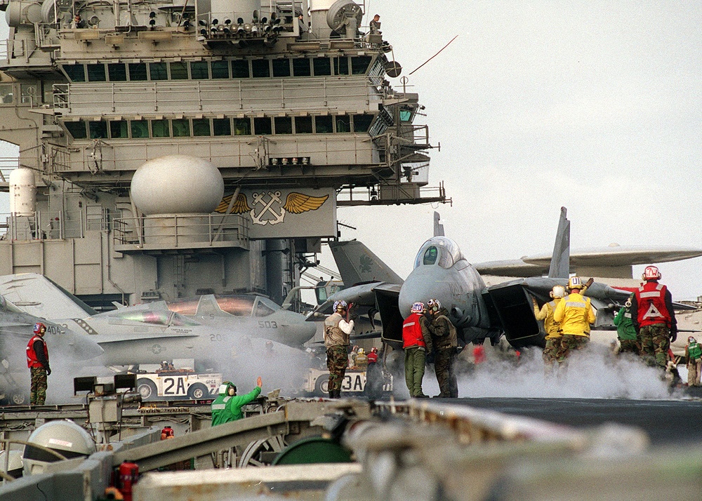 Steam rises from a previous catapult launch as an F-14 Tomcat is directed into position for launch from the flight deck of the USS Constellation.