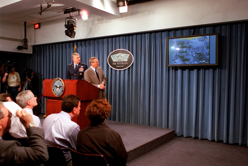 Secretary Rumsfeld watches the television screen as Gen. Myers describes the area hit during a Pentagon news briefing.