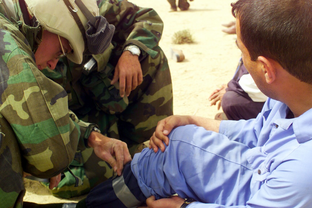 U.S. Marines assist a captured enemy prisoner of war in the desert of Iraq.
