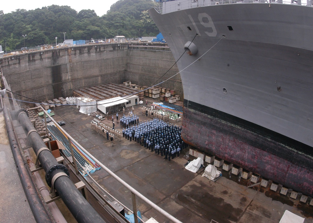Crewmembers of the USS Blue Ridge (LCC 19) are dwarfed by the bow of their ship.