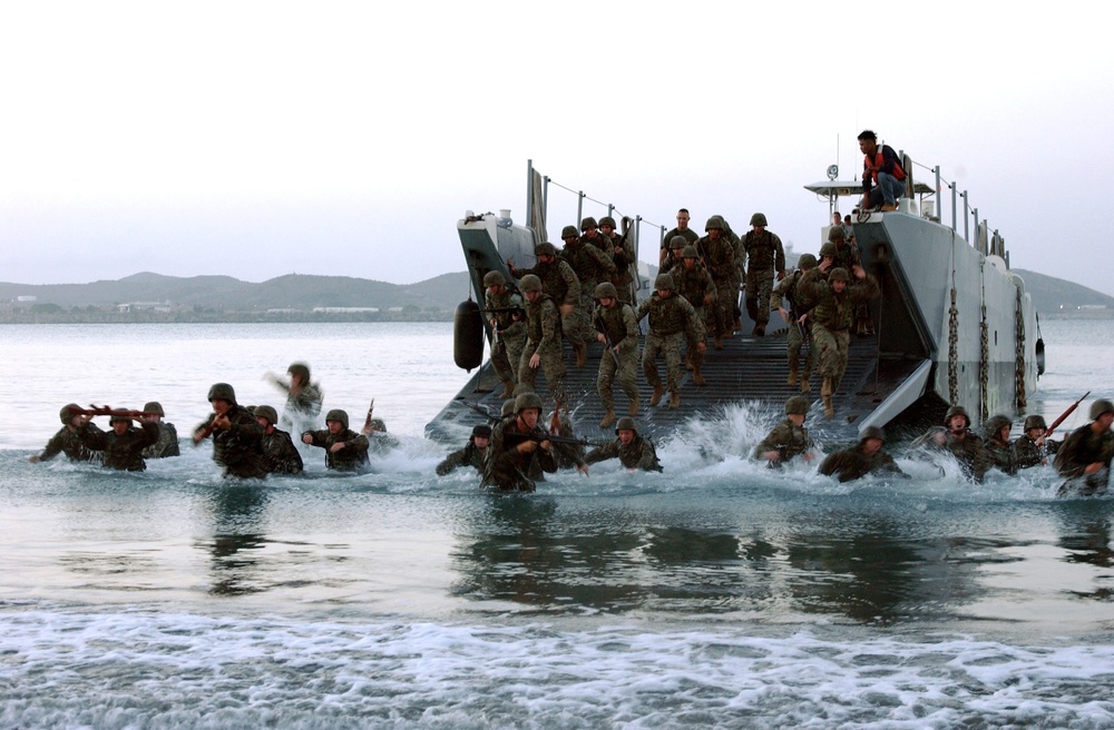 U.S. Marines and sailors jump out of their landing craft and plunge into the surf.