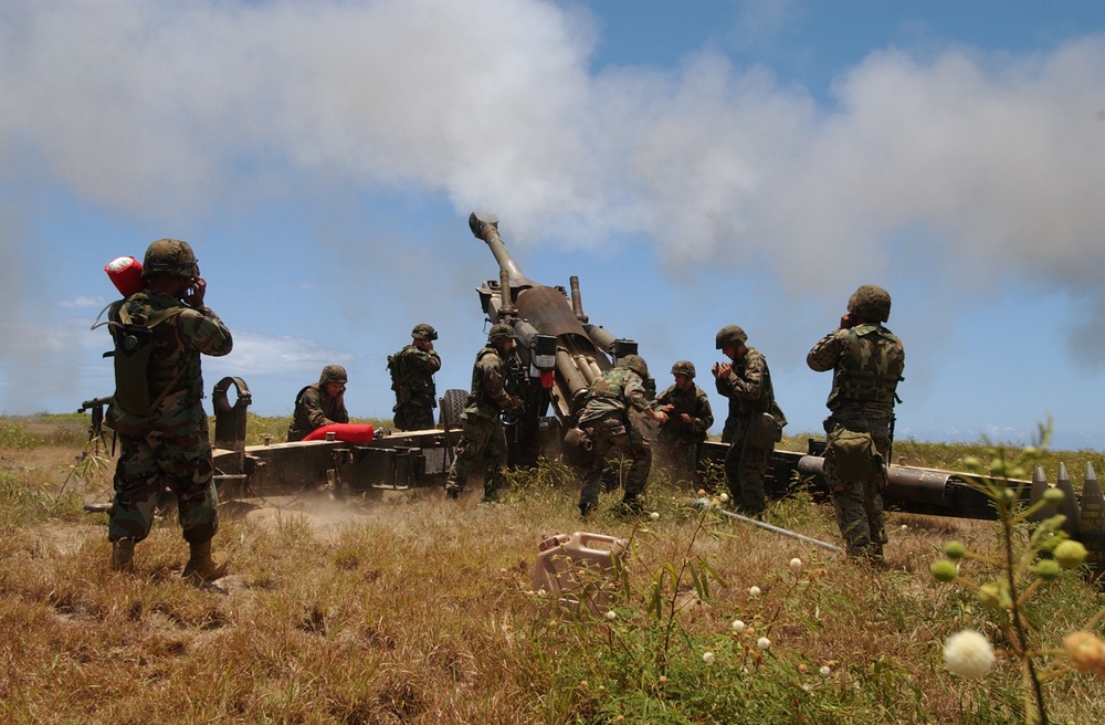 Marines cover their ears as a round is fired from a M198 155mm Medium Howitzer.