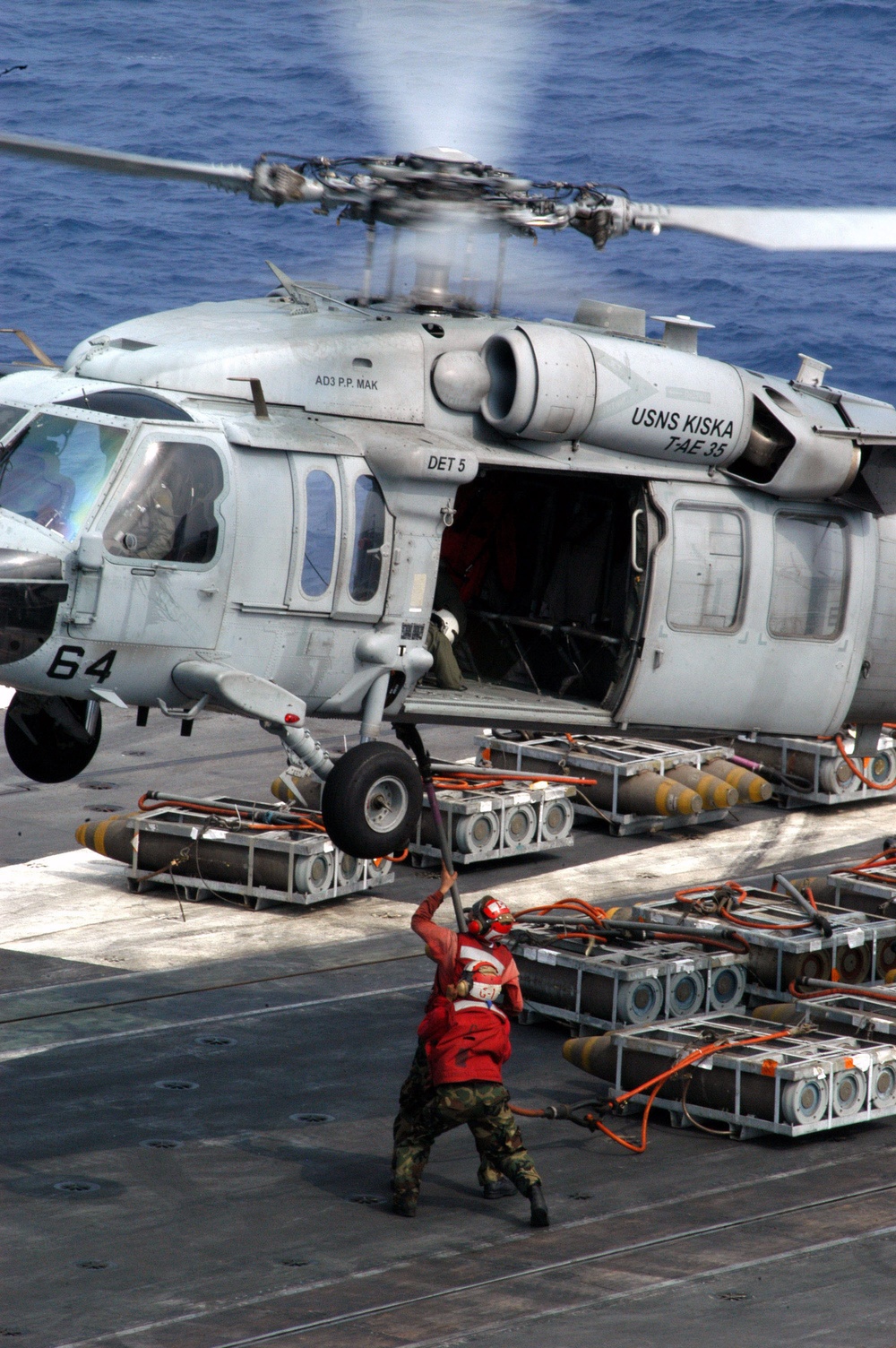Aviation ordnancemen hold a cargo tether steady for connection to an HH-60 Seahawk.