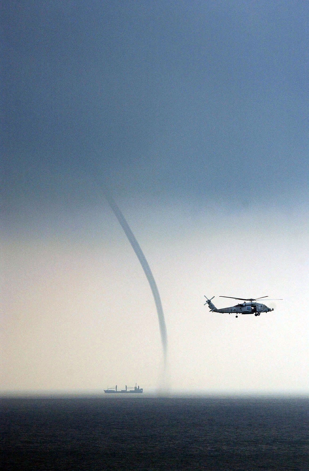 A Navy HH-60H Seahawk helicopter keeps a wary eye on a nearby vessel and a waterspout.