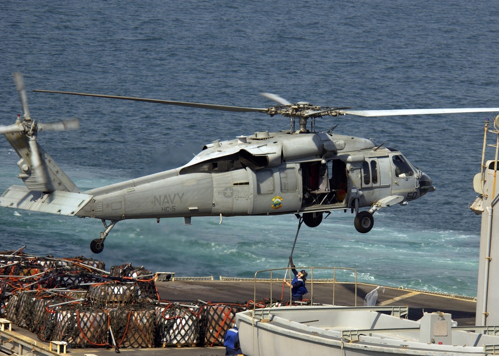 A sailor aboard the USS Seattle (AOE 3) attaches a cargo sling to the hook of an SH-60 Seahawk.