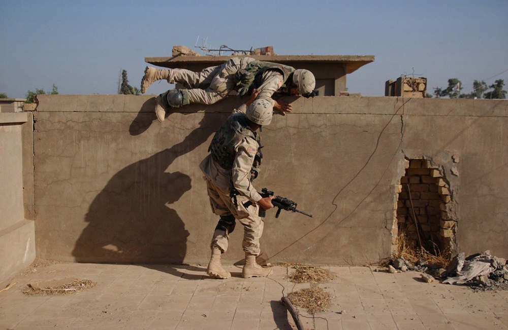 A U.S. Army soldier helps another over a wall.