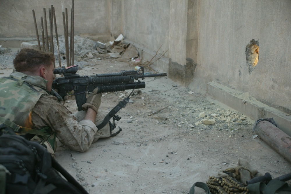 A U.S. Marine watches through a hole in the wall.