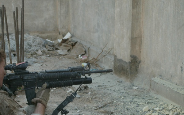 A U.S. Marine watches through a hole in the wall.