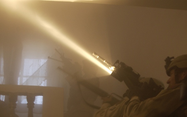 The beam of a flashlight fastened to a rifle cuts through the dust.