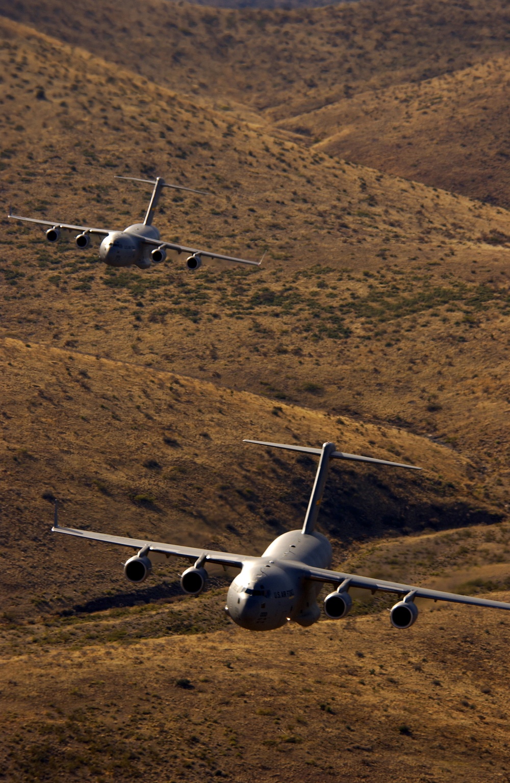 Two U.S. Air Force C-17 Globemasters III fly at low levels.