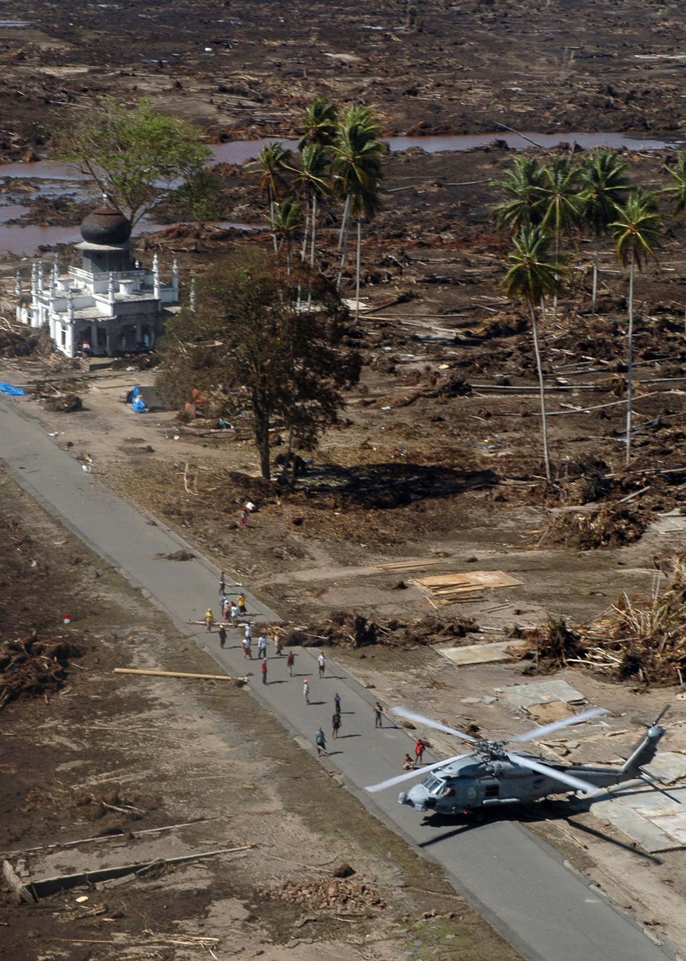 Indonesian citizens run toward a U.S. Navy SH-60 Seahawk helicopter.