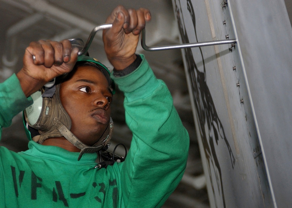 Petty Officer 3rd Class Willie Brown unscrews bolts from a panel on an F/A-18C Hornet.