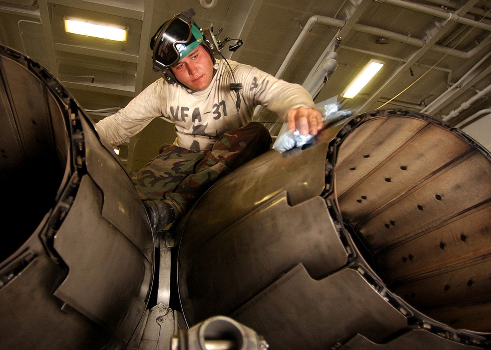 Petty Officer 2nd Class Christopher Shamblin wipes down the jet engine afterburner vanes on an F/A-18C Hornet.