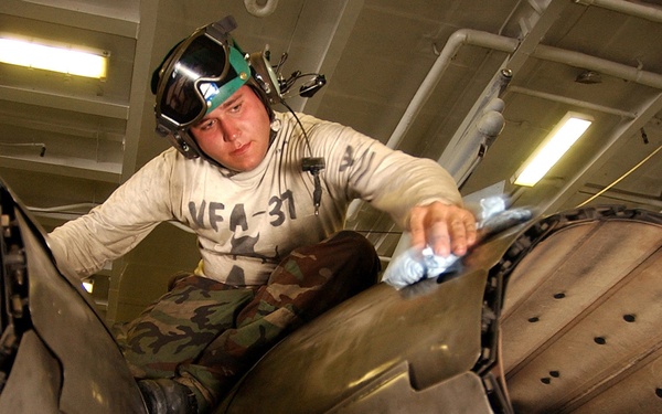 Petty Officer 2nd Class Christopher Shamblin wipes down the jet engine afterburner vanes on an F/A-18C Hornet.