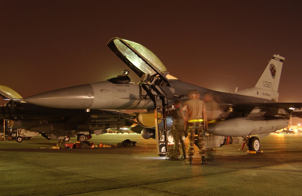 The slow shutter speed required for this night photograph blurs the air and ground crew members as they prepare to launch an F-16 Fight Falcon.