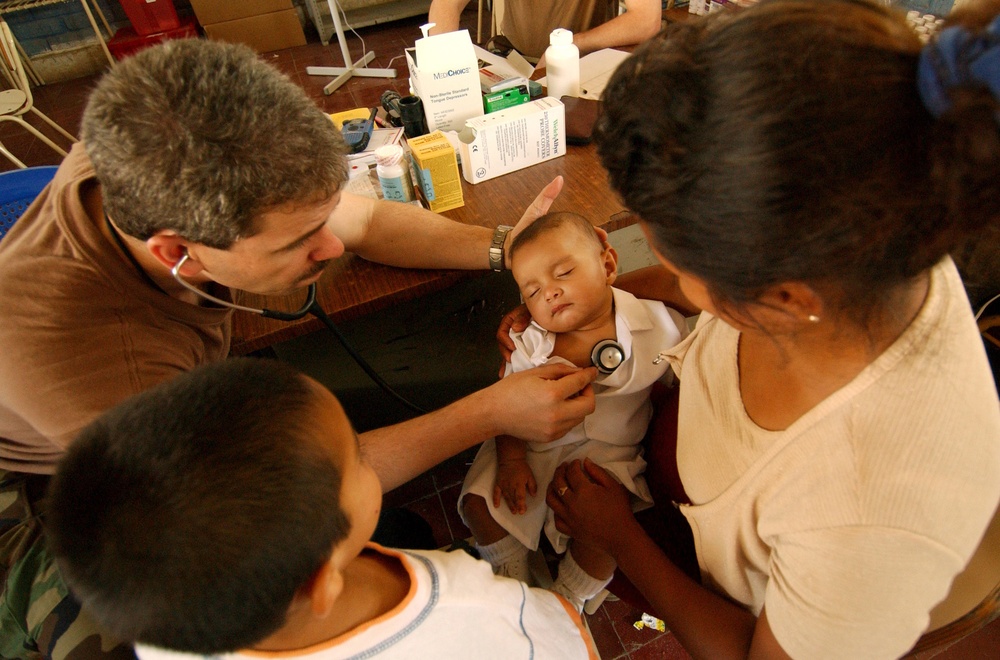 U.S. Navy Cmdr. Ron Hicks uses his stethoscope to listen to the heart of a baby.