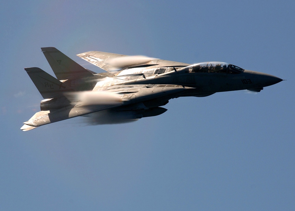 Clouds of water vapor rush over the swept-wings of a Navy F-14B Tomcat as it performs a high-speed fly-by.