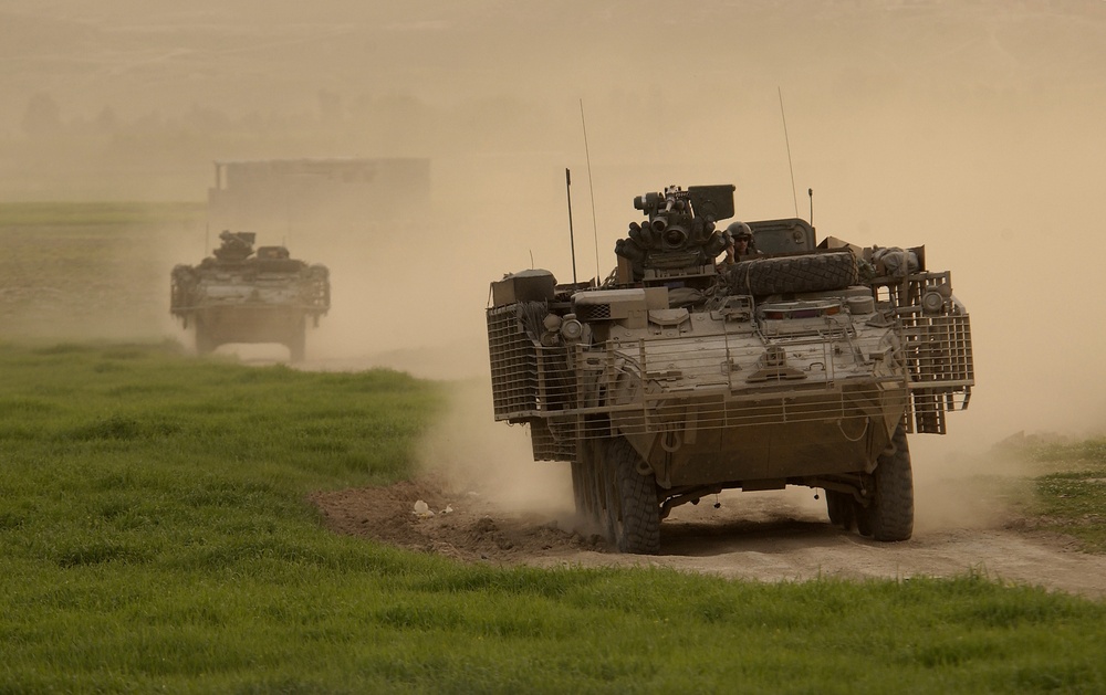 Army Stryker vehicles of the Stryker Brigade Combat Team kick up plumes of dust.