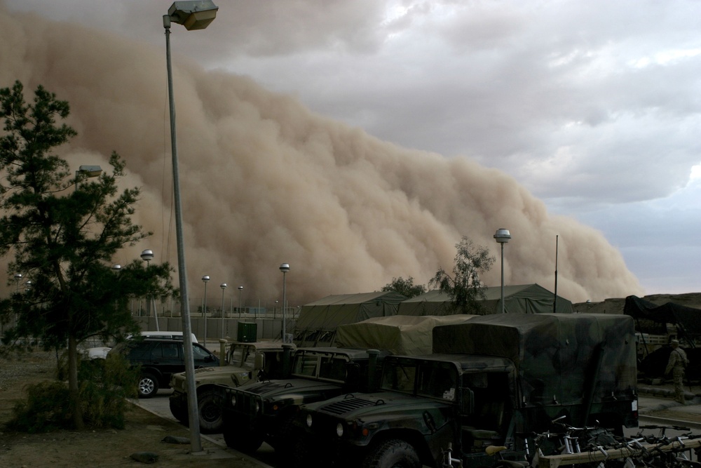 A massive sand storm cloud is close to enveloping a military camp.