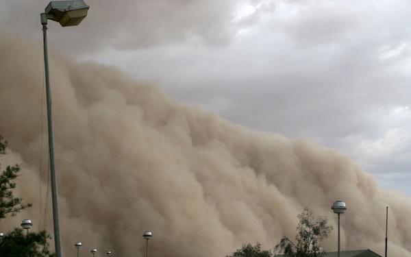 A massive sand storm cloud is close to enveloping a military camp.