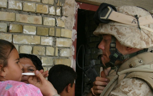 Navy Hospitalman Kevin Crim uses a thermometer to check the temperature of a sick Iraqi child.