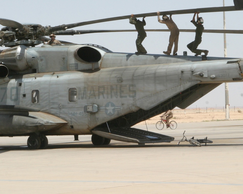 Three Marines perform a balancing act as they lift a rotor blade of a CH-53 Super Stallion.