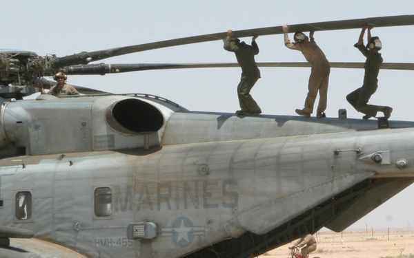 Three Marines perform a balancing act as they lift a rotor blade of a CH-53 Super Stallion.