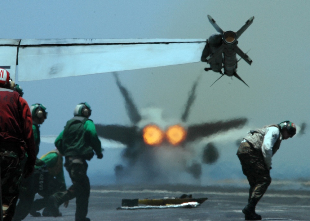 The afterburners of an F/A-18C Hornet bathe the flight deck in heat waves.