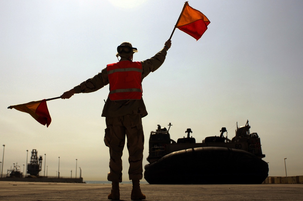 Navy Seaman Charles Shafer uses flags to signal to the craftmaster of a Navy Landing Craft Air Cushion.