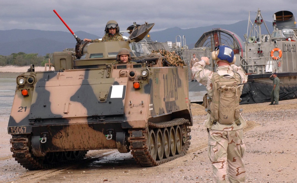 A Navy beachmaster directs an Australian armored personnel carrier on the beach.