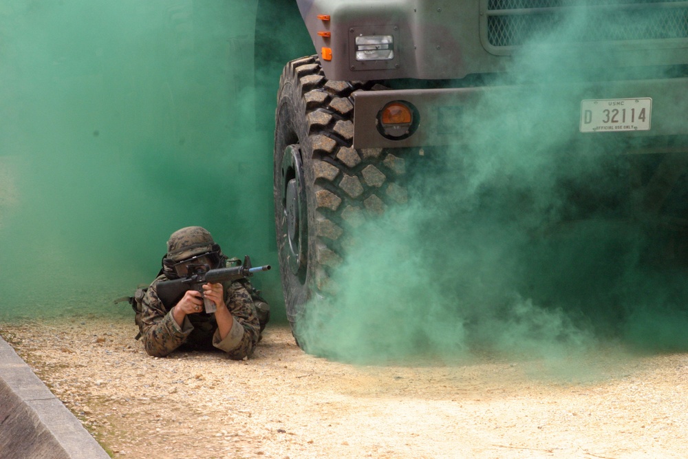 A U.S. Marine uses the cover of a truck and green smoke.