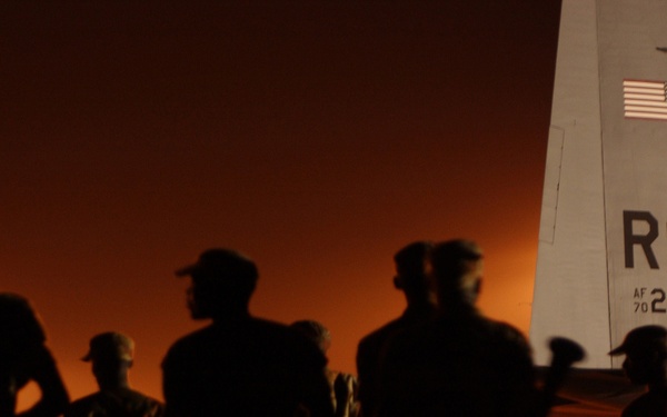 Rwandan soldiers are bathed in the lights of the flight line.