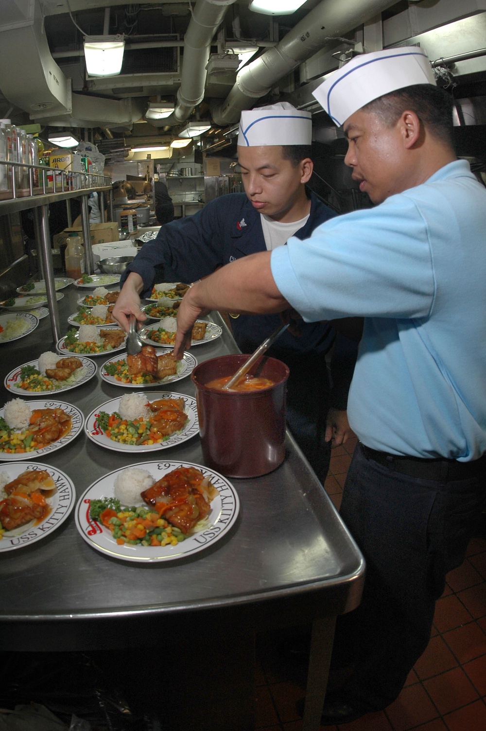Petty Officer 1st Class Rogelio Magpantay and Petty Officer 2nd Class Gomer Cubol prepare entrees for a ward room dinner.