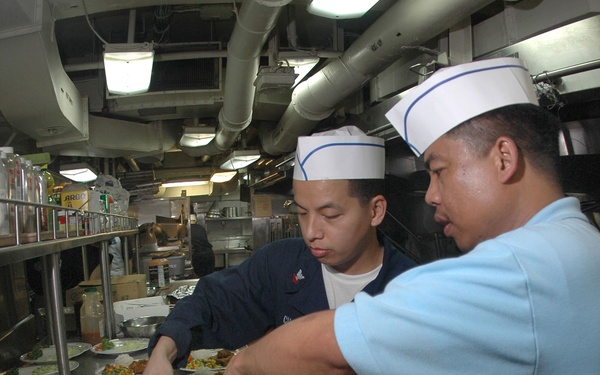 Petty Officer 1st Class Rogelio Magpantay and Petty Officer 2nd Class Gomer Cubol prepare entrees for a ward room dinner.