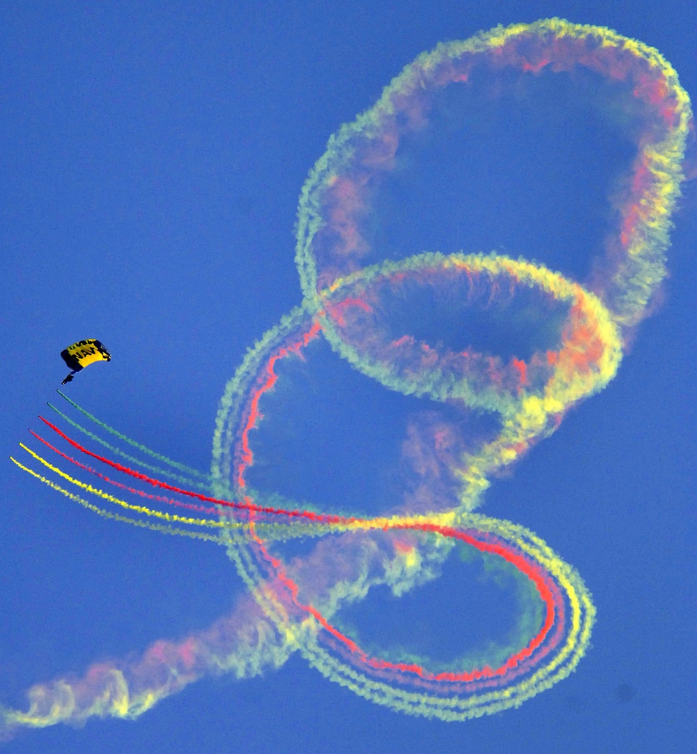A member of the U.S. Navy Parachute Team fills the sky with colored smoke.