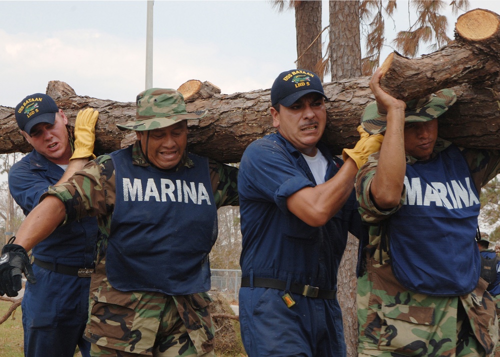 U.S. Navy sailors and Mexican Marines carry a log as they remove Hurricane Katrina debris.